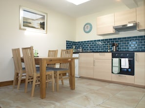 A kitchen with a dining table, chairs, a clock, cabinets, and a tiled backsplash.