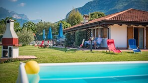 Ein Poolbereich mit Liegestühlen und Sonnenschirmen, ein Gebäude mit einem Ziegeldach und Berge im Hintergrund.