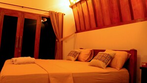 A hotel room with a bed, curtains, and wooden paneling on the walls. - Macoa Village (Gili Trawangan)
