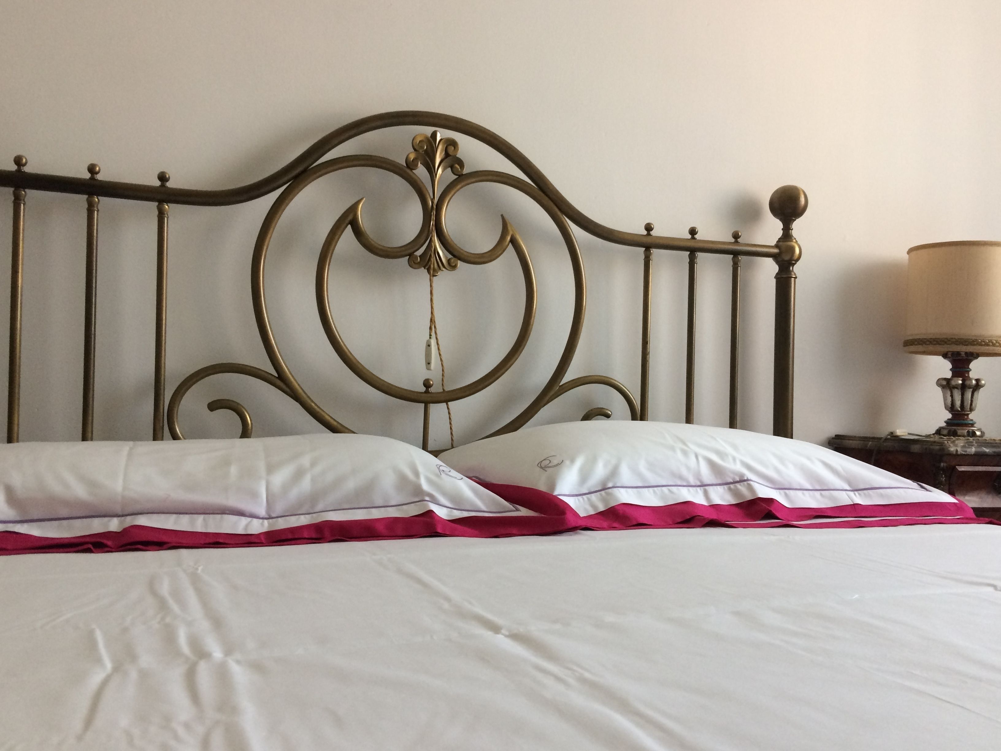 Ein Bett mit Metall-Kopfteil, weißer Bettwäsche und einer roten Decke.