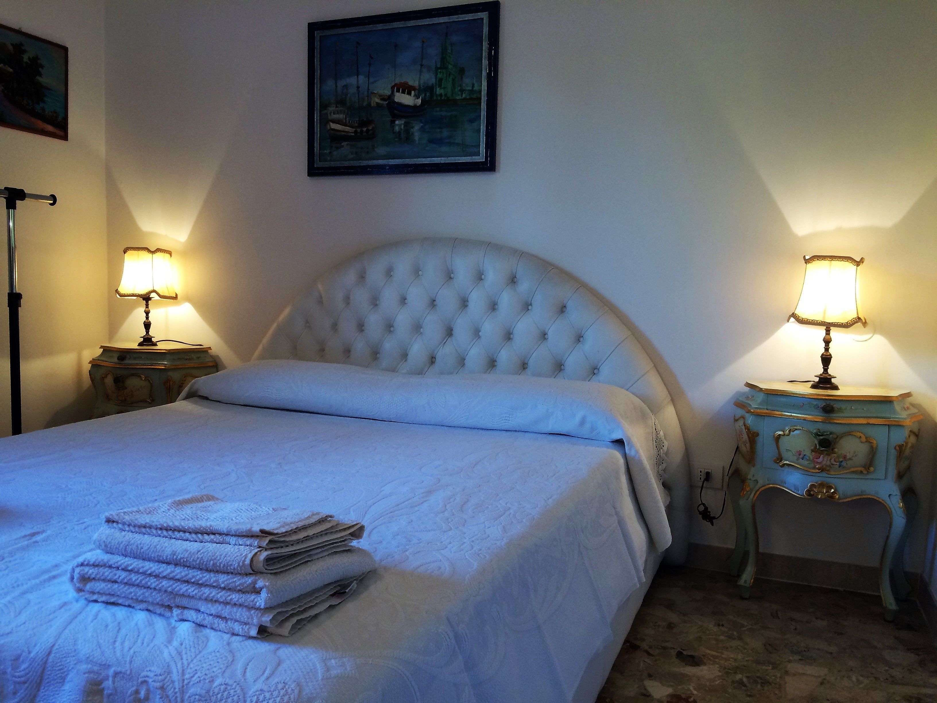 A neatly made bed with a tufted headboard, two bedside tables with lamps, and a painting on the wall.