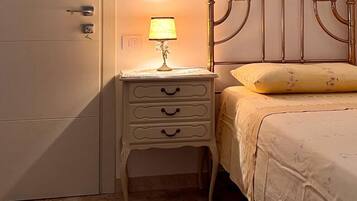 Un dormitorio con cama, mesita de noche con lámpara, mesita auxiliar y armario.