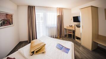 A hotel room with a bed, a desk, a chair, a television, and a wardrobe.