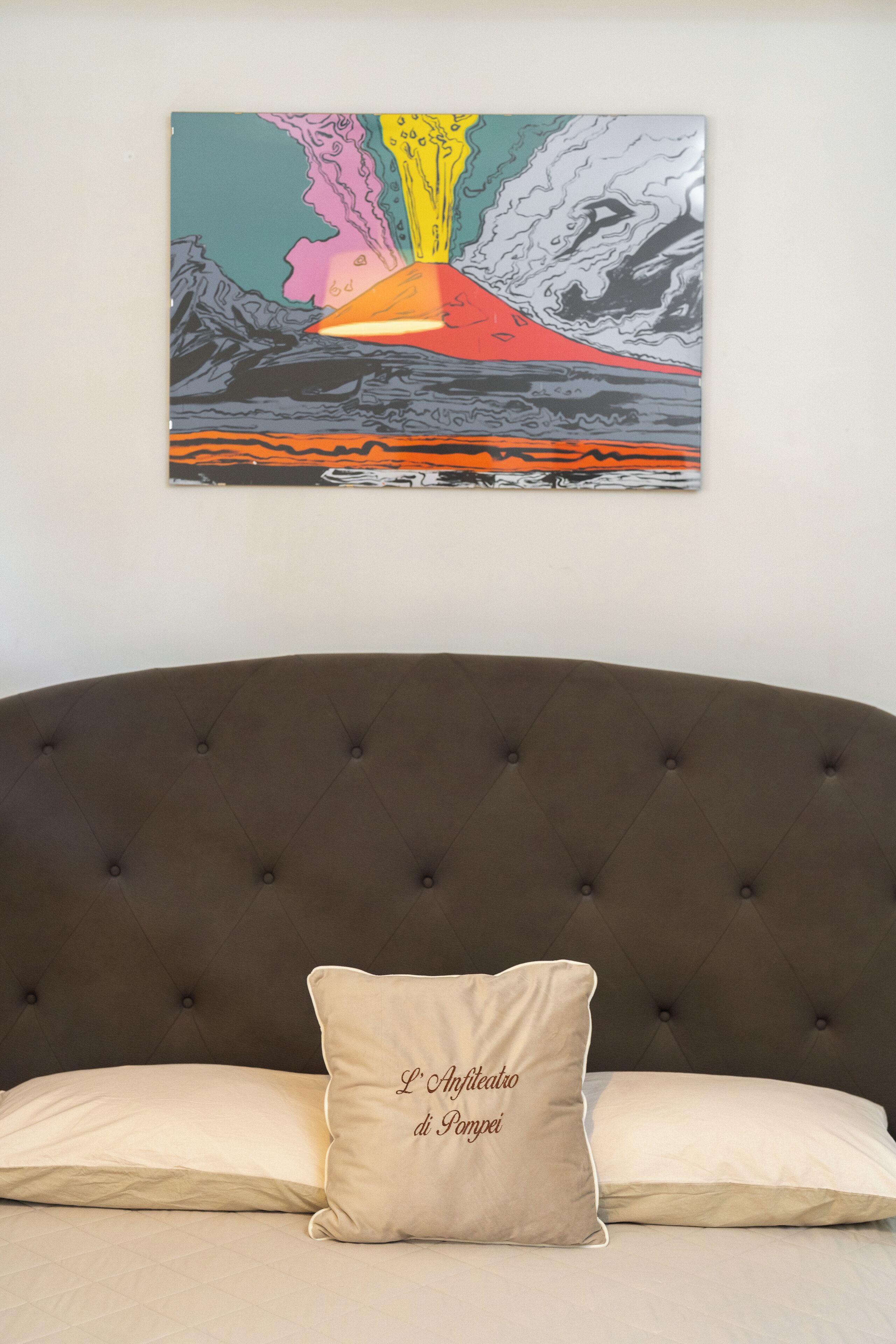 A bedroom with a tufted headboard, a bed with two pillows, and a colorful abstract painting on the wall.