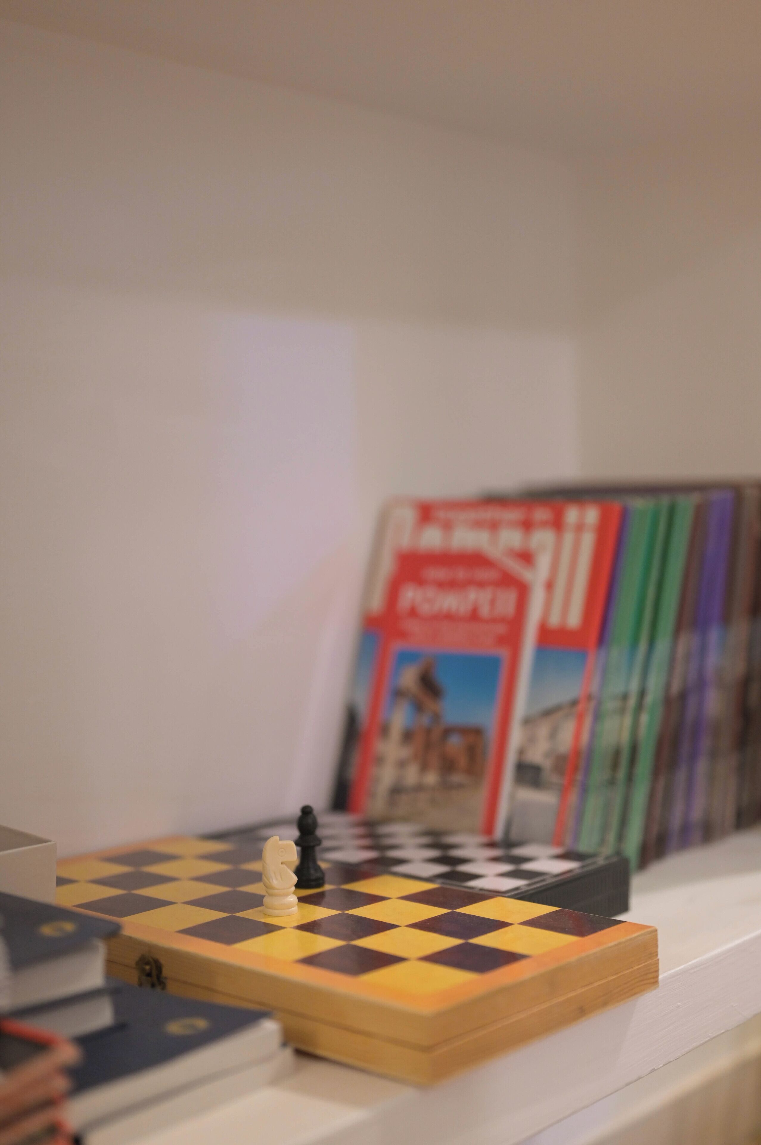 Un échiquier posé sur une étagère, avec des livres en arrière-plan.