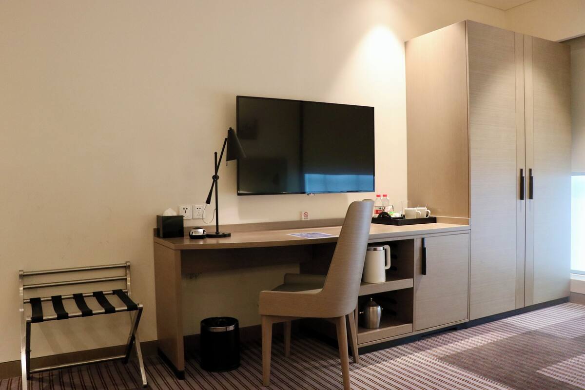 A hotel room with a desk, chair, TV, and wardrobe.
