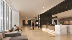 Een moderne lobby met zithoeken, een receptiebalie en een groot raam dat voor natuurlijk licht zorgt.
