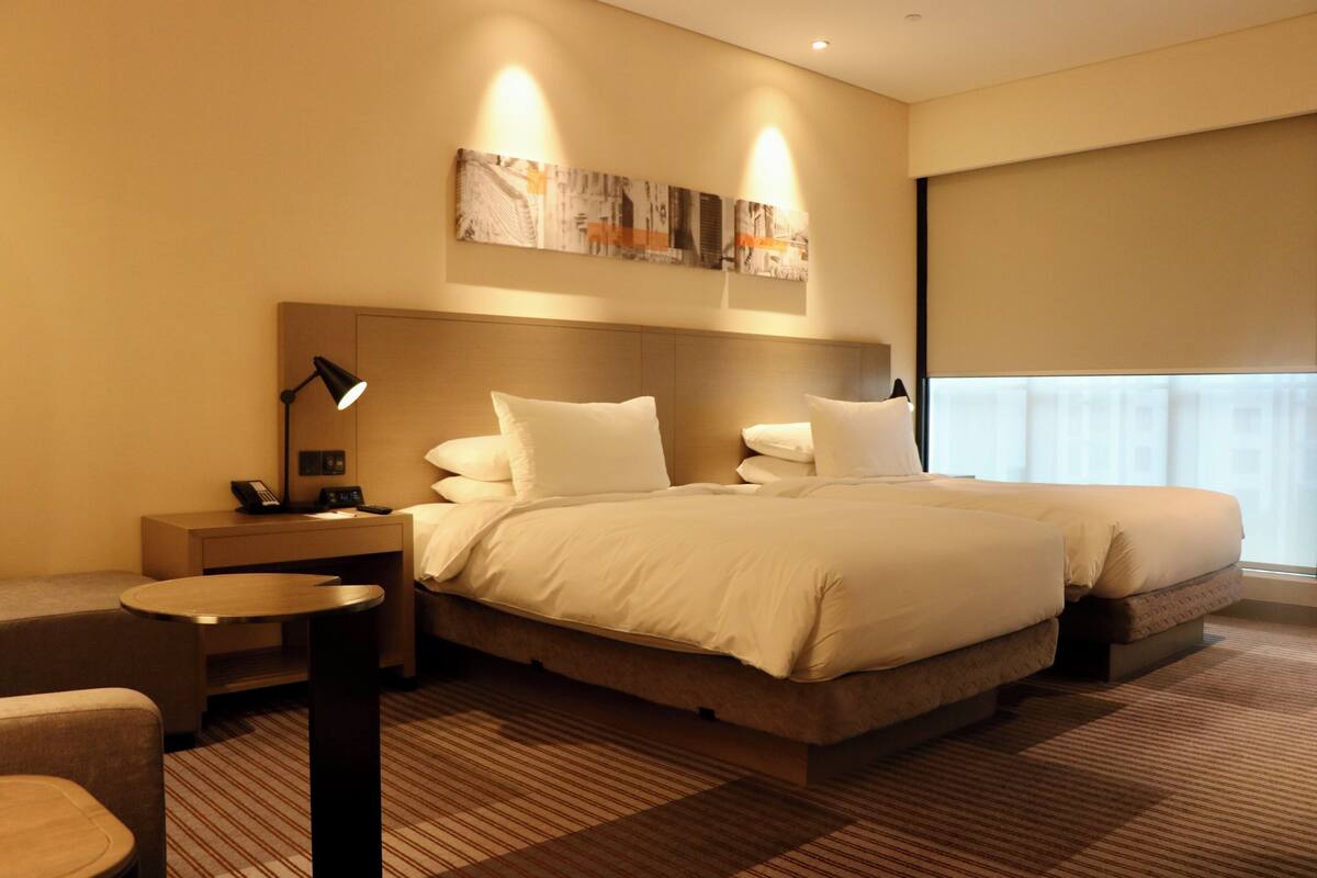 A hotel room with a large bed, a bedside table with a lamp, a small round table, and a wall-mounted artwork.
