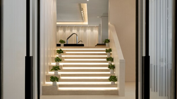 Een moderne trap met geïntegreerde verlichting en beplanting, die leidt naar een goed verlichte binnenruimte.