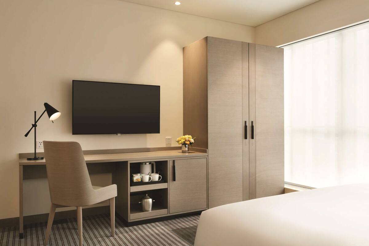 A hotel room with a bed, a desk with a chair, a television, a cabinet, and a window with curtains.