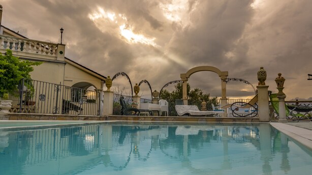 A swimming pool with a decorative fence, lounge chairs, and a building with a balcony.