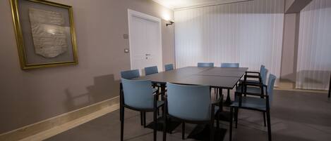 A conference room with a rectangular table, six chairs, a framed picture on the wall, a door, and a window with blinds.