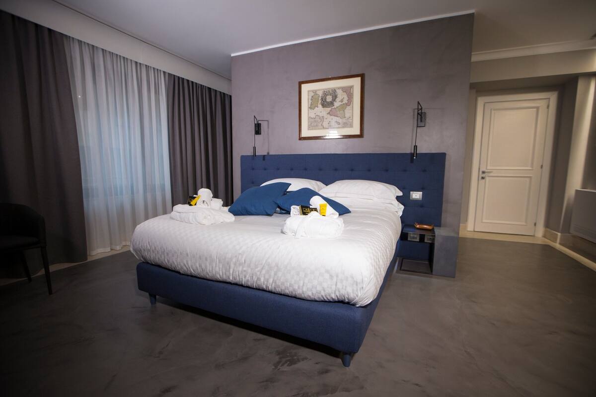 A modern hotel room with a large bed, a headboard, a framed map on the wall, and a door to the right.