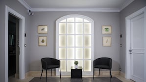 A room with a large arched window, two black chairs, a small table with a plant, and framed pictures on the walls. - Principessa Mafalda (Messina)