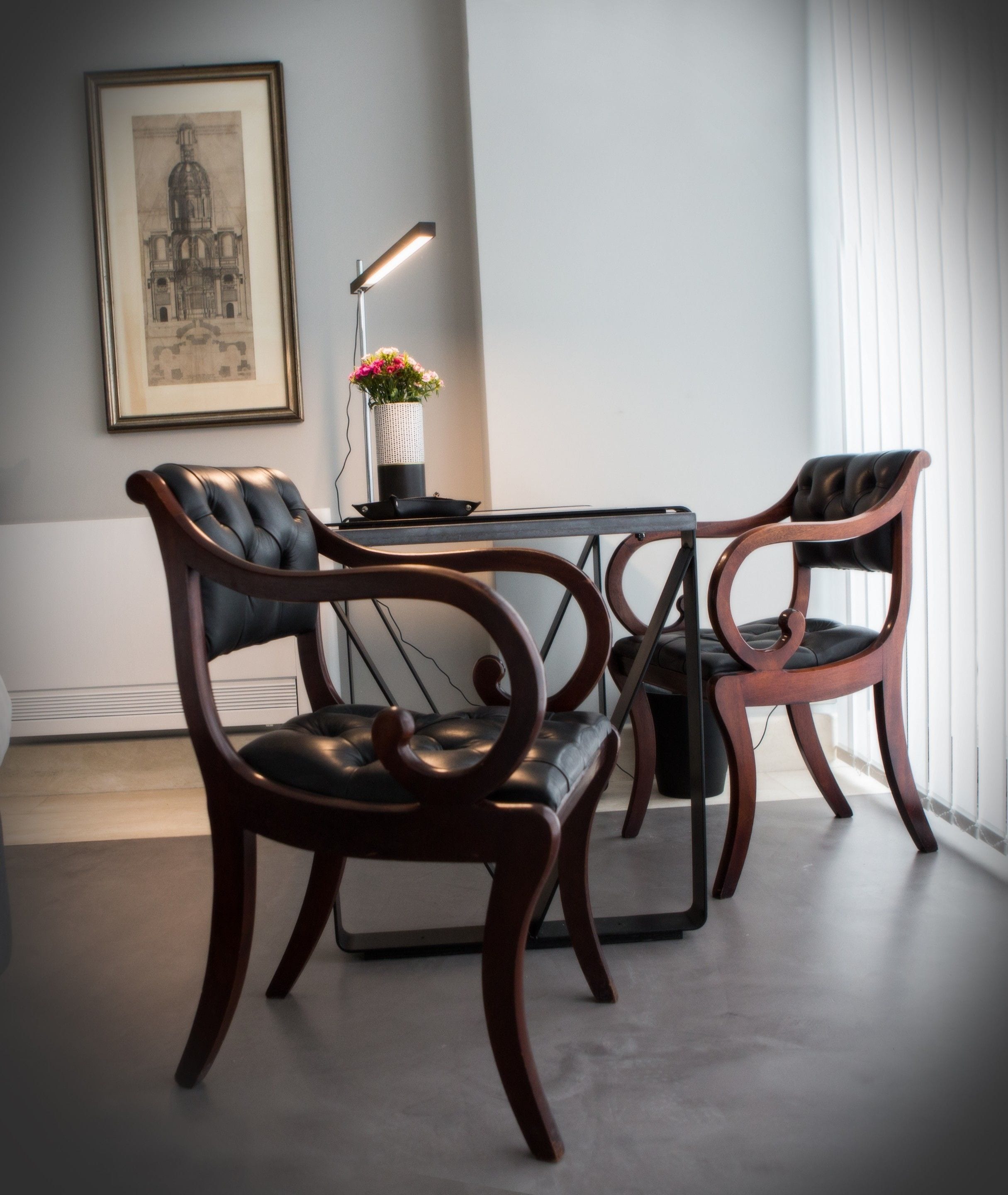 Una habitación moderna con una mesa de vidrio, dos sillones de cuero, un cuadro enmarcado y un florero con flores.