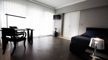 A modern bedroom with a bed, bedside table, chair, and a TV mounted on the wall.