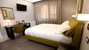A hotel room with a bed, a desk, a chair, a TV, a lamp, and a window with curtains.