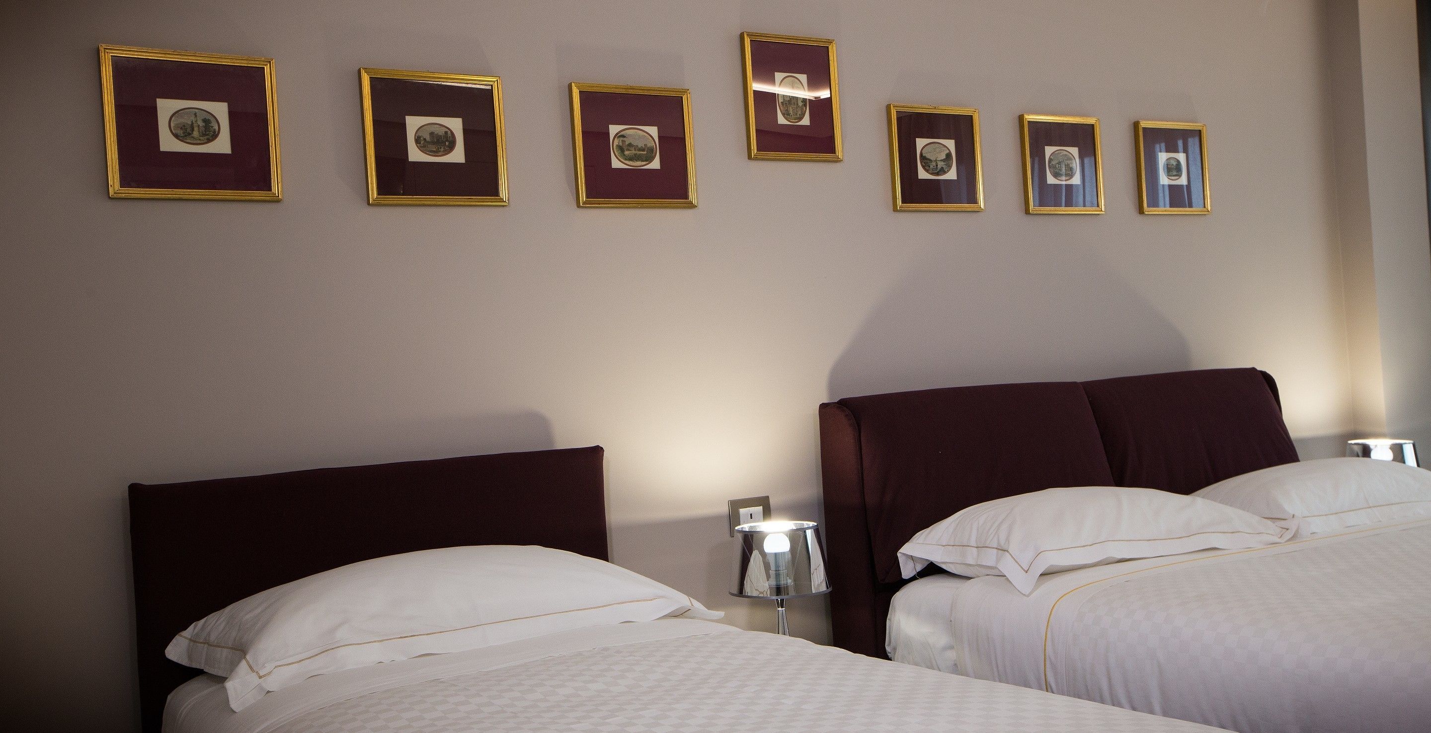 A hotel room with two beds, a headboard, a nightstand, and framed pictures on the wall.