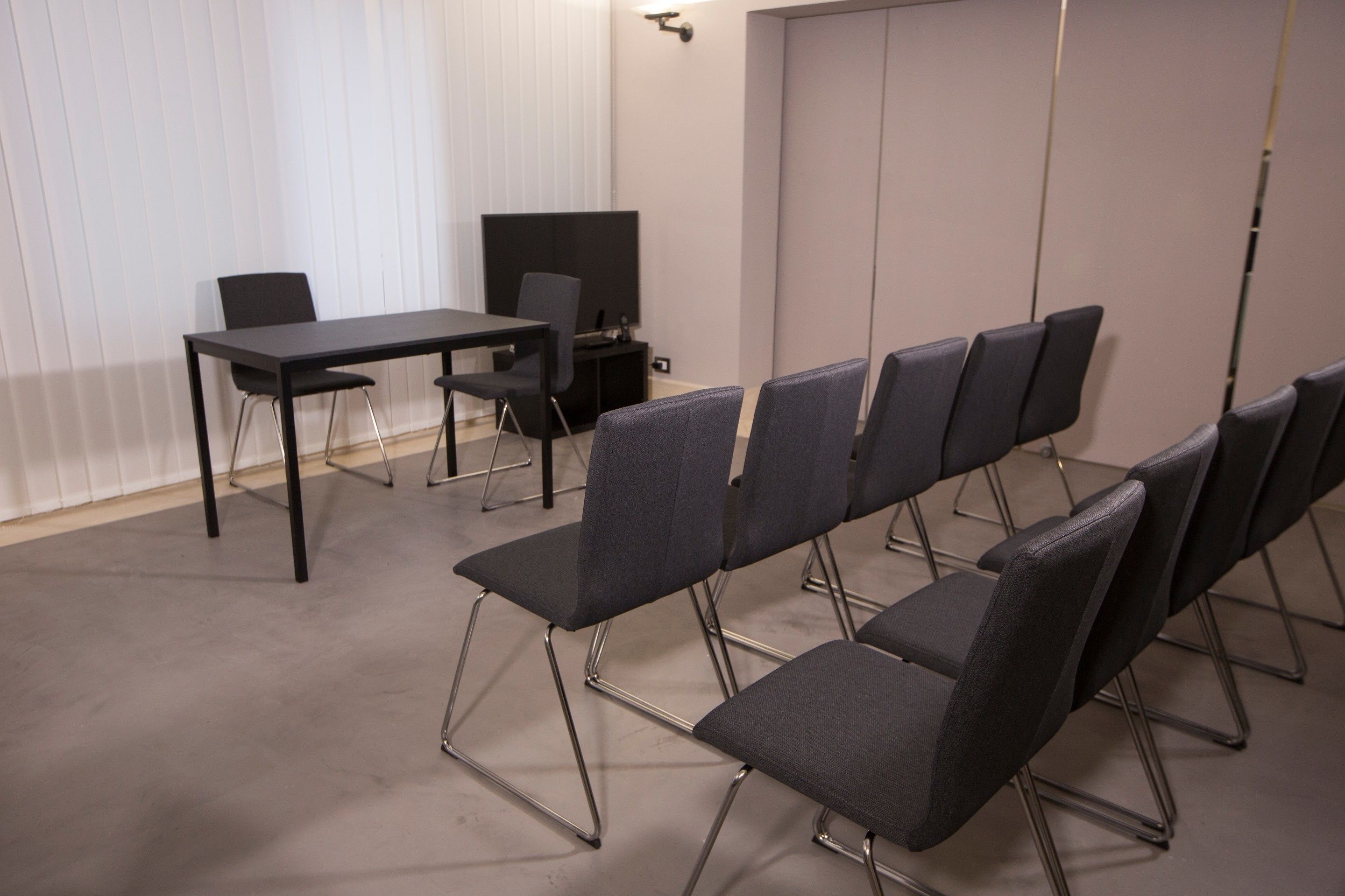 Una sala de conferencias con una mesa, sillas, una televisión y una puerta cerrada.