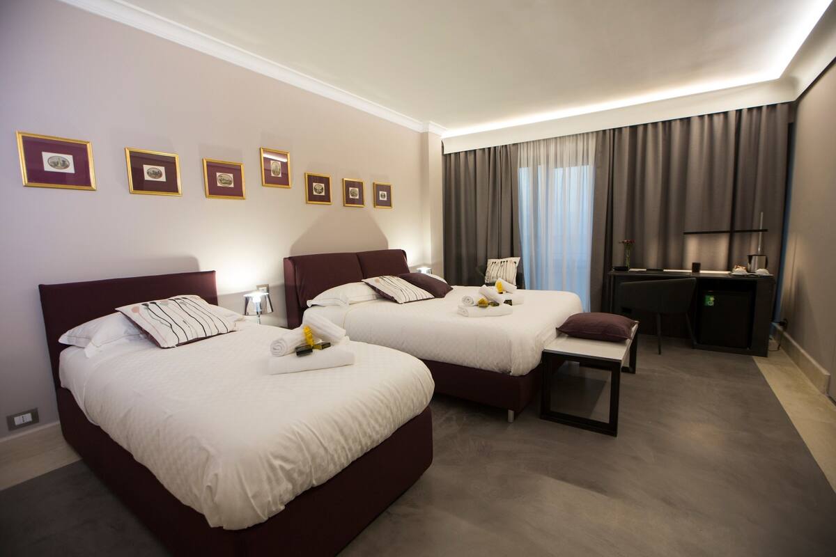 A hotel room with two beds, a desk, a chair, and a TV.