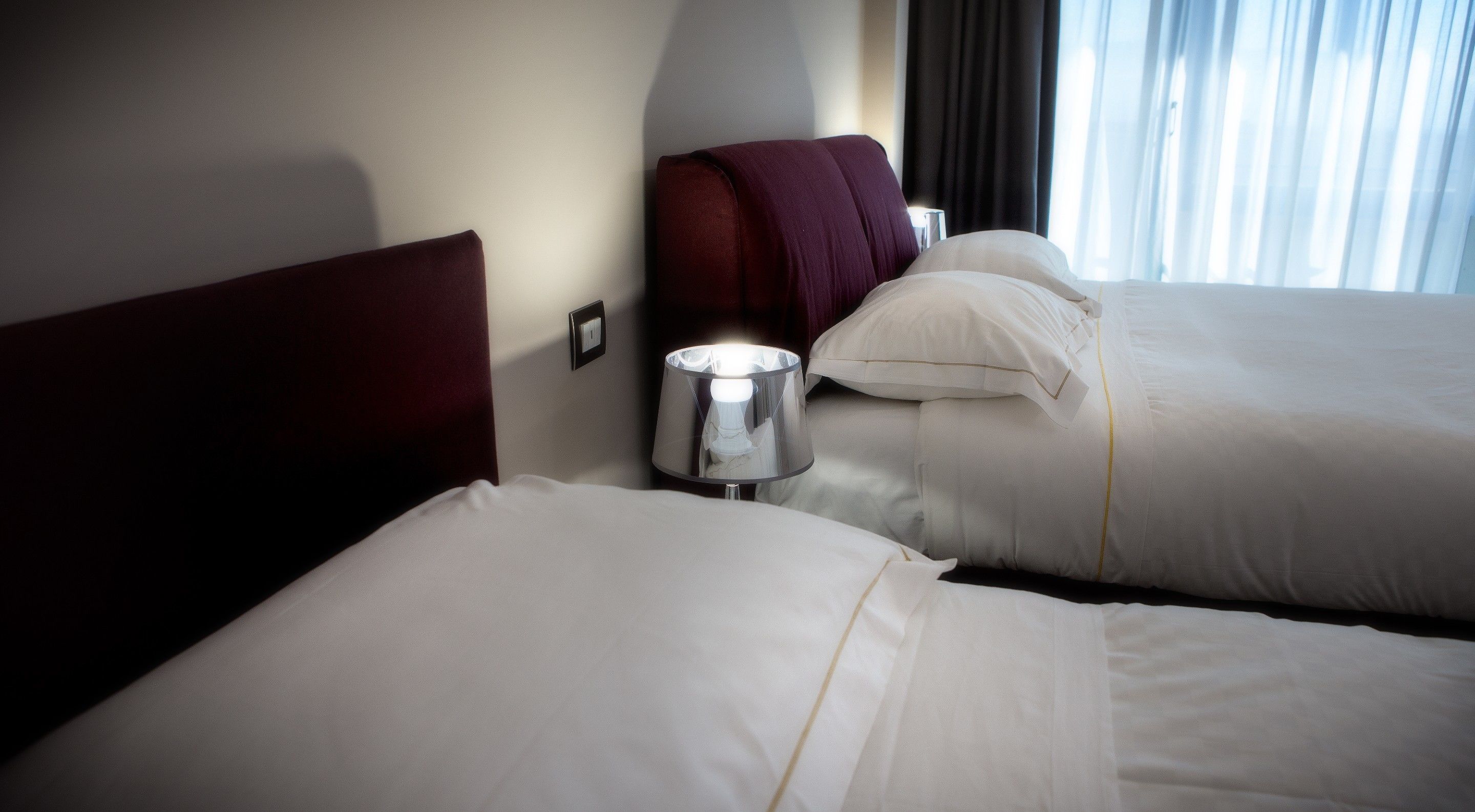 Habitación de hotel con dos camas, una lámpara y un ventanal con cortinas.