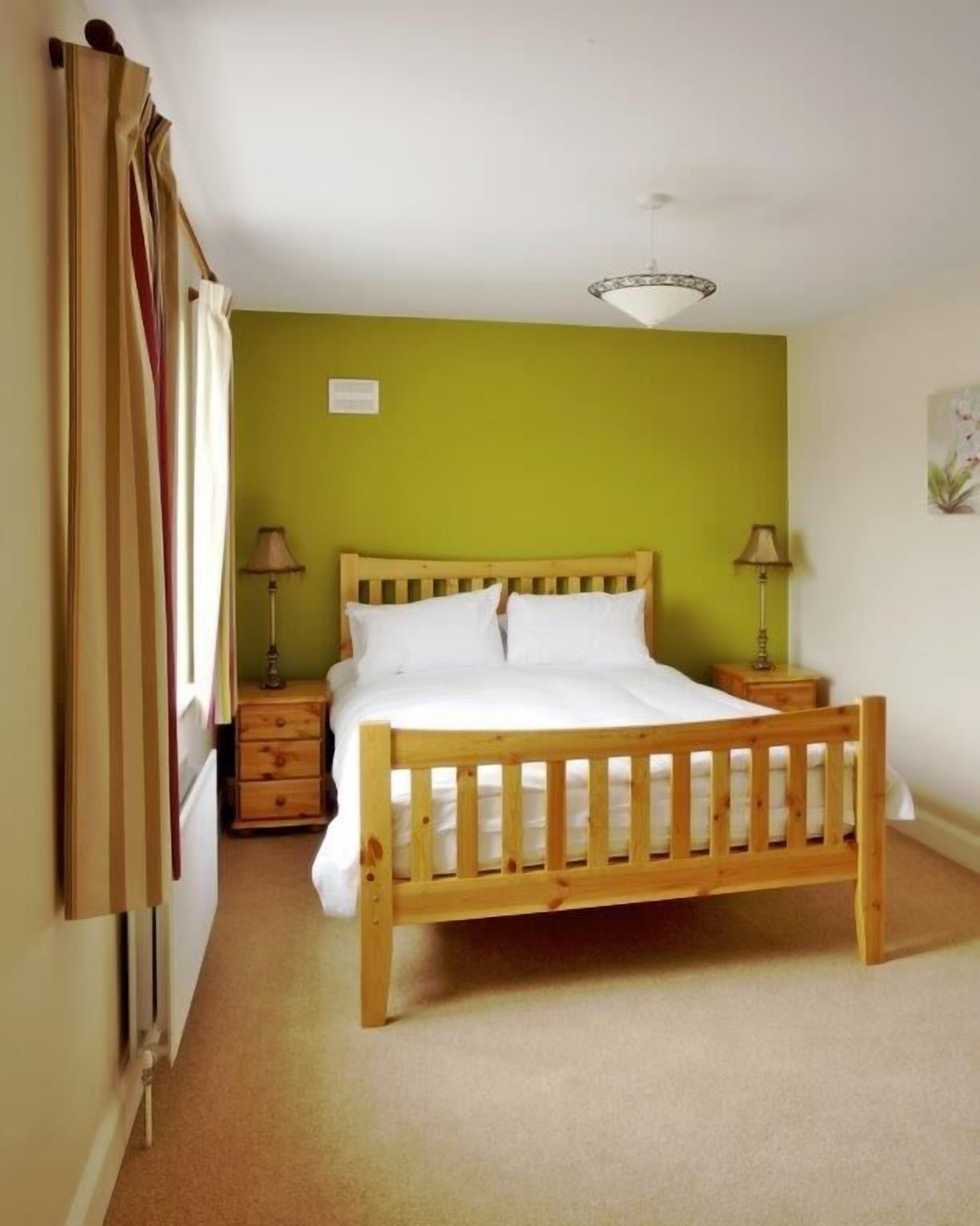 A bedroom with a wooden bed, two bedside tables, a nightstand, and a window with curtains.