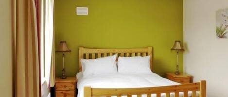 A bedroom with a wooden bed, two bedside tables, a nightstand, and a window with curtains.