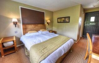 A hotel room with a large bed, two bedside tables, a chair, and a door.