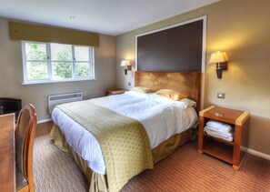 A hotel room with a large bed, two bedside lamps, a nightstand with a lamp, a chair, and a view of greenery through the window. - The Narrowboat At Weedon (Northampton)