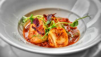 A dish with seared scallops, garnished with microgreens and herbs, served on a white plate.
