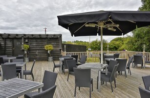An outdoor deck with tables and chairs, a large umbrella, and a wooden fence.