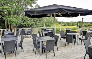 An outdoor patio with tables and chairs, a black umbrella, and a view of trees and a field.