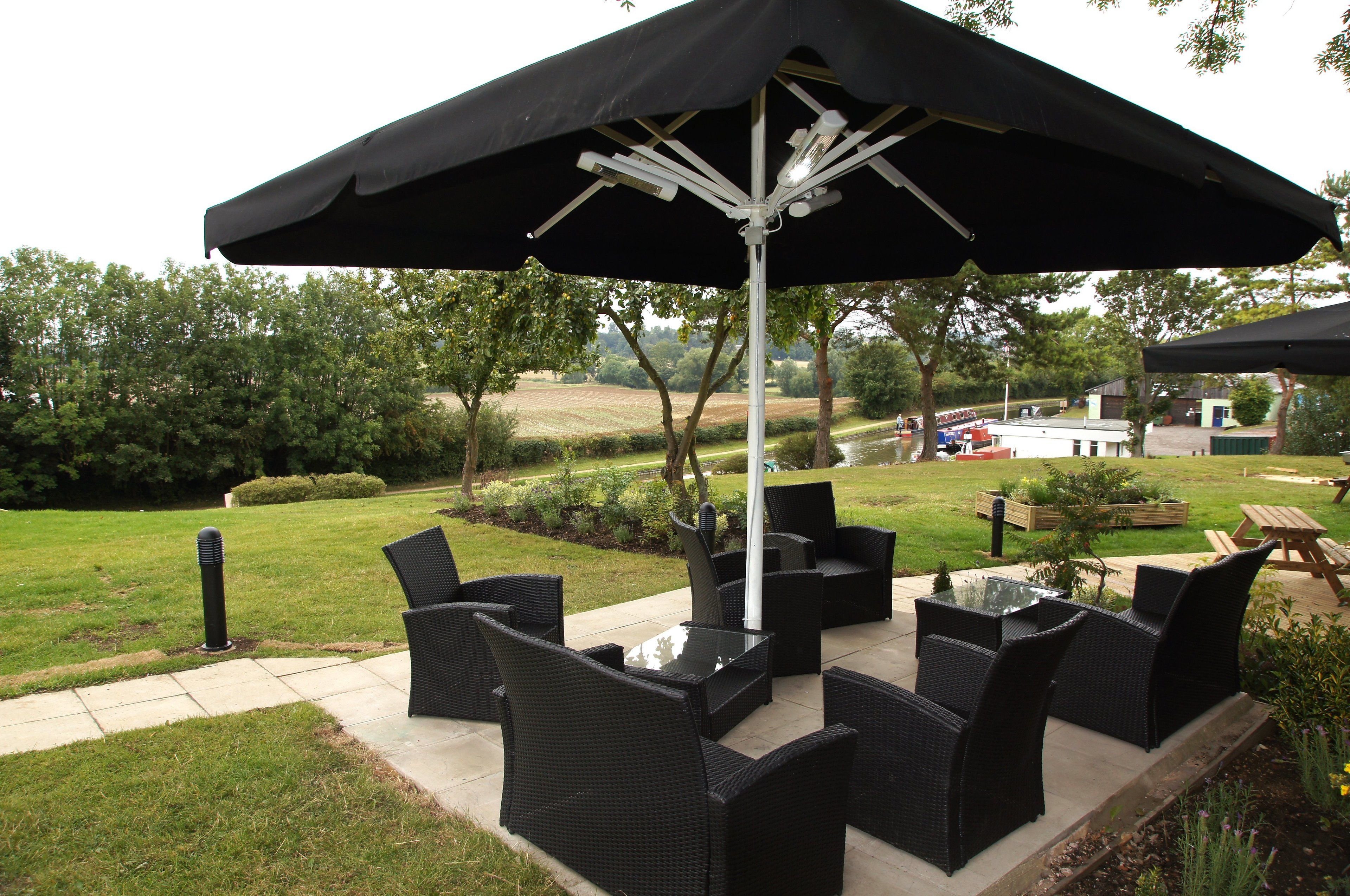 Un área de patio al aire libre con mobiliario de mimbre, una mesa de vidrio y un gran paraguas.