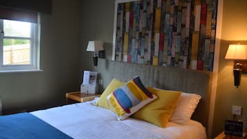 A hotel room with a bed, a wall art piece, a window, a nightstand, and a sign.