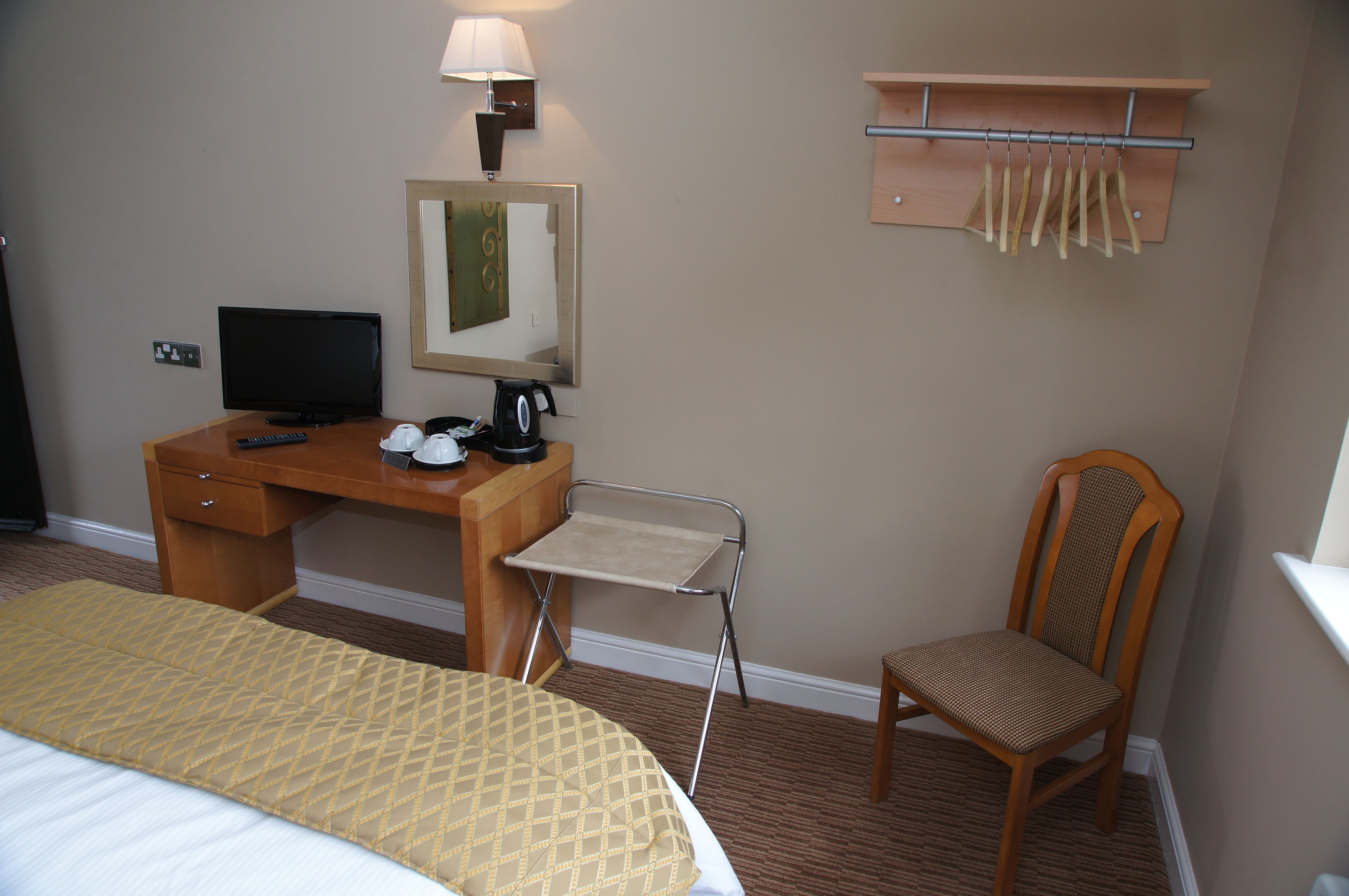 A hotel room with a bed, a desk with a computer, a chair, a small table with a coffee maker, a mirror, and a coat rack.