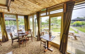 A dining area with wooden tables and chairs, large windows, and a view of the outdoor patio. - The Narrowboat At Weedon (Northampton)
