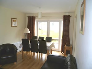 Ein Wohnzimmer mit einem schwarzen Ledersofa, einem Esstisch mit Stühlen, einer Lampe und Blick durch eine Glastür.