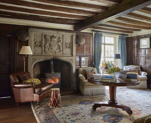 A traditional room with a fireplace, leather armchair, and a round wooden table with books and a vase. - Harlington Manor (Dunstable)