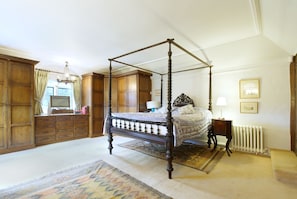 A four-poster canopy bed in a room with wooden paneling, a radiator, and a large rug. - Harlington Manor (Dunstable)