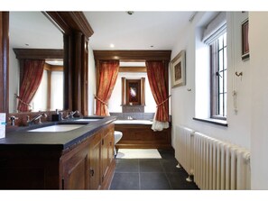 A bathroom with a double sink vanity, a large mirror, and a radiator. - Harlington Manor (Dunstable)