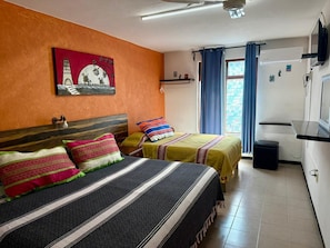 Ein Hotelzimmer mit zwei Betten, einem Wandbild, einem Fenster mit Vorhängen und einer Küchenzeile.