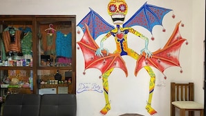 A room with a large wall mural of a colorful skeleton with wings, a wooden chair, a small round table, and a black leather sofa.