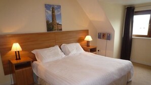 A bedroom with a large bed, two bedside tables with lamps, a wooden headboard, and a painting on the wall. - Shanagarry Holiday Village (Shanagarry)