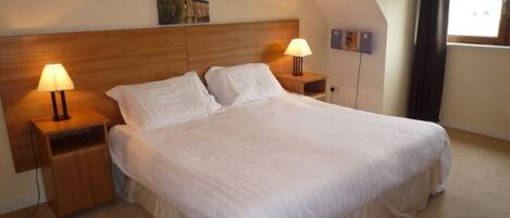 Un dormitorio con una cama grande, dos mesitas de noche con lámparas, un cabecero de madera y un cuadro en la pared.
