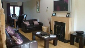 A living room with a fireplace, a television, and a dining area in the background. - Shanagarry Holiday Village (Shanagarry)