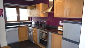 A compact kitchen with wooden cabinets, a dishwasher, a washing machine, an oven, and a refrigerator. - Shanagarry Holiday Village (Shanagarry)