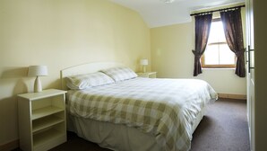 A single-bed room with a checkered bedspread, a bedside table with a lamp, and a window with curtains. - Ballylickey Bay Holiday Home (Bantry)