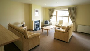 A living room with beige sofas, a wooden coffee table, a TV, and a fireplace. - Ballylickey Bay Holiday Home (Bantry)