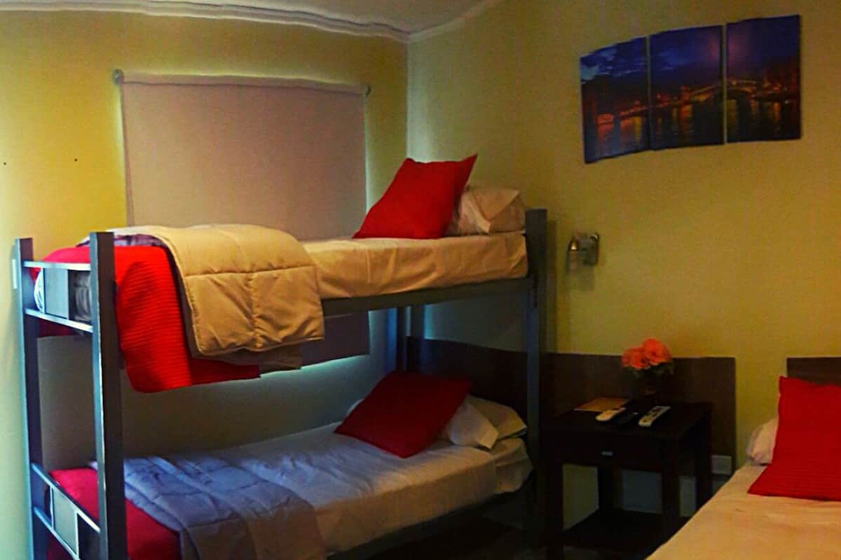 A hotel room with two bunk beds, a single bed, a nightstand with a vase of flowers, and a wall-mounted artwork.
