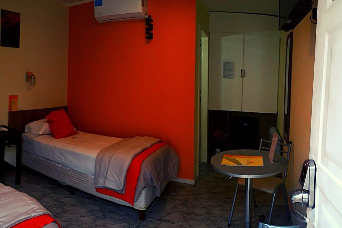 A hotel room with two beds, a small table, a chair, a TV, and a wardrobe.